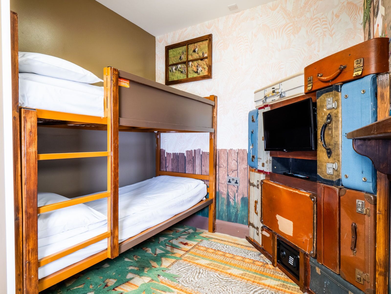 A bunk bed with a wooden frame and a mattress, a television on a wooden cabinet, and a patterned rug on the floor.
