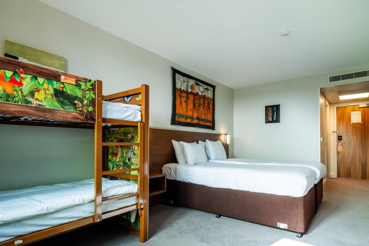 A hotel room with bunk beds, a single bed, a painting on the wall, and a door.