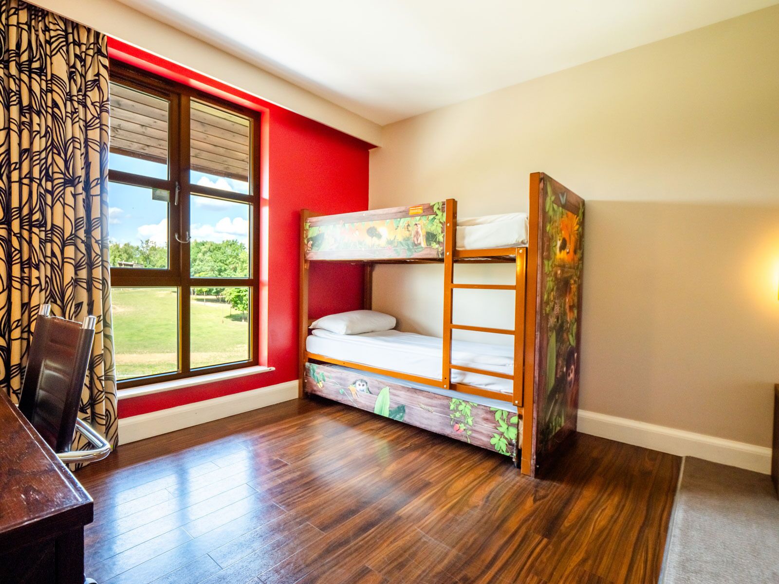 Habitació amb lliteres, escriptori i finestra amb vista a vegetació.