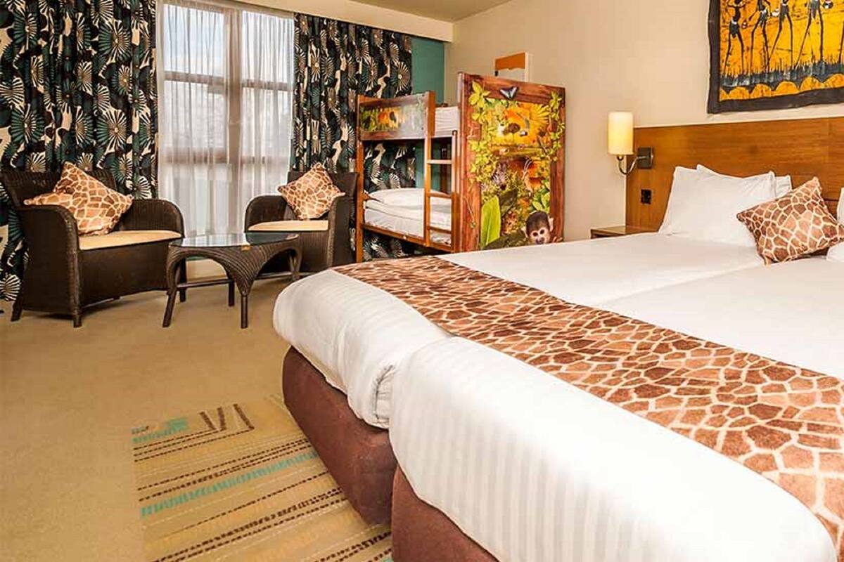 A hotel room with a large bed, a desk, a chair, and a painting on the wall.