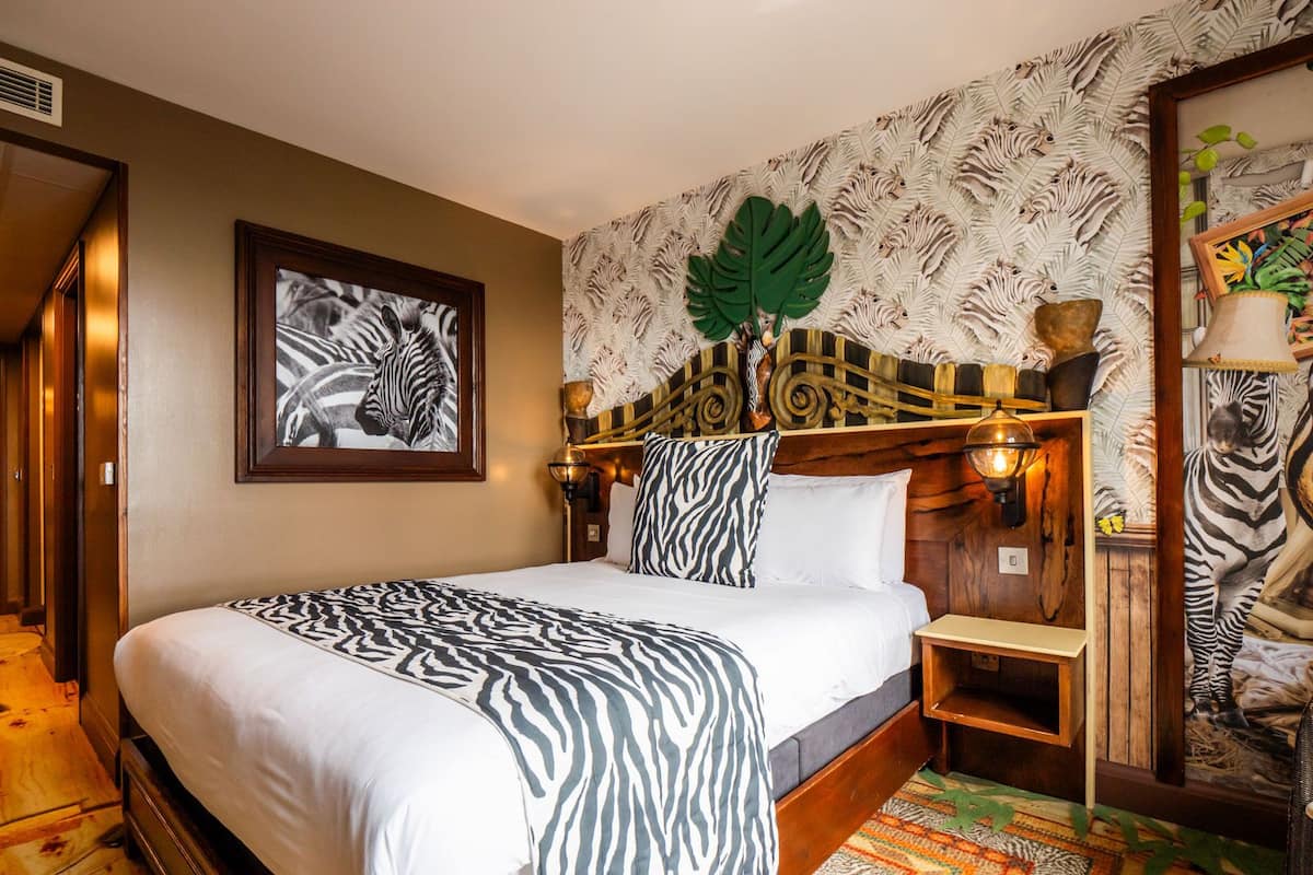 A room with a zebra-patterned bedspread, a framed zebra artwork on the wall, a decorative leaf on the headboard, and a zebra-themed lamp.