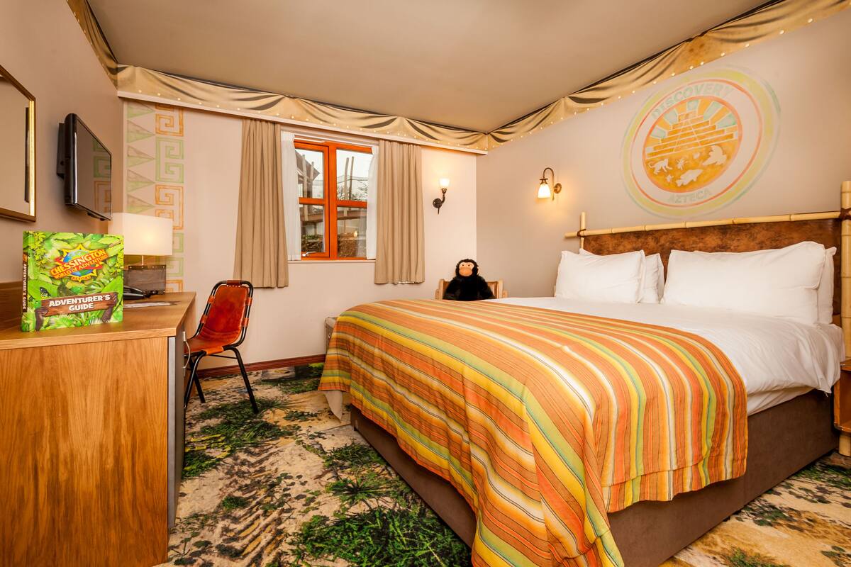 A hotel room with a bed, a desk, a chair, a TV, and a window with curtains.