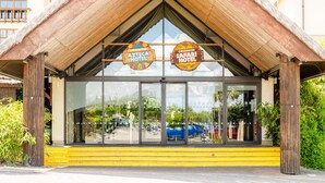 The entrance of the Chessington Safari Hotel with a thatched roof and large glass windows reflecting the surrounding area. - Chessington Resort Hotel (Chessington)