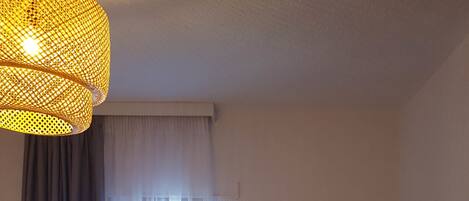 Un dormitorio moderno con cama, escritorio, silla, televisor y un amplio ventanal con cortinas.