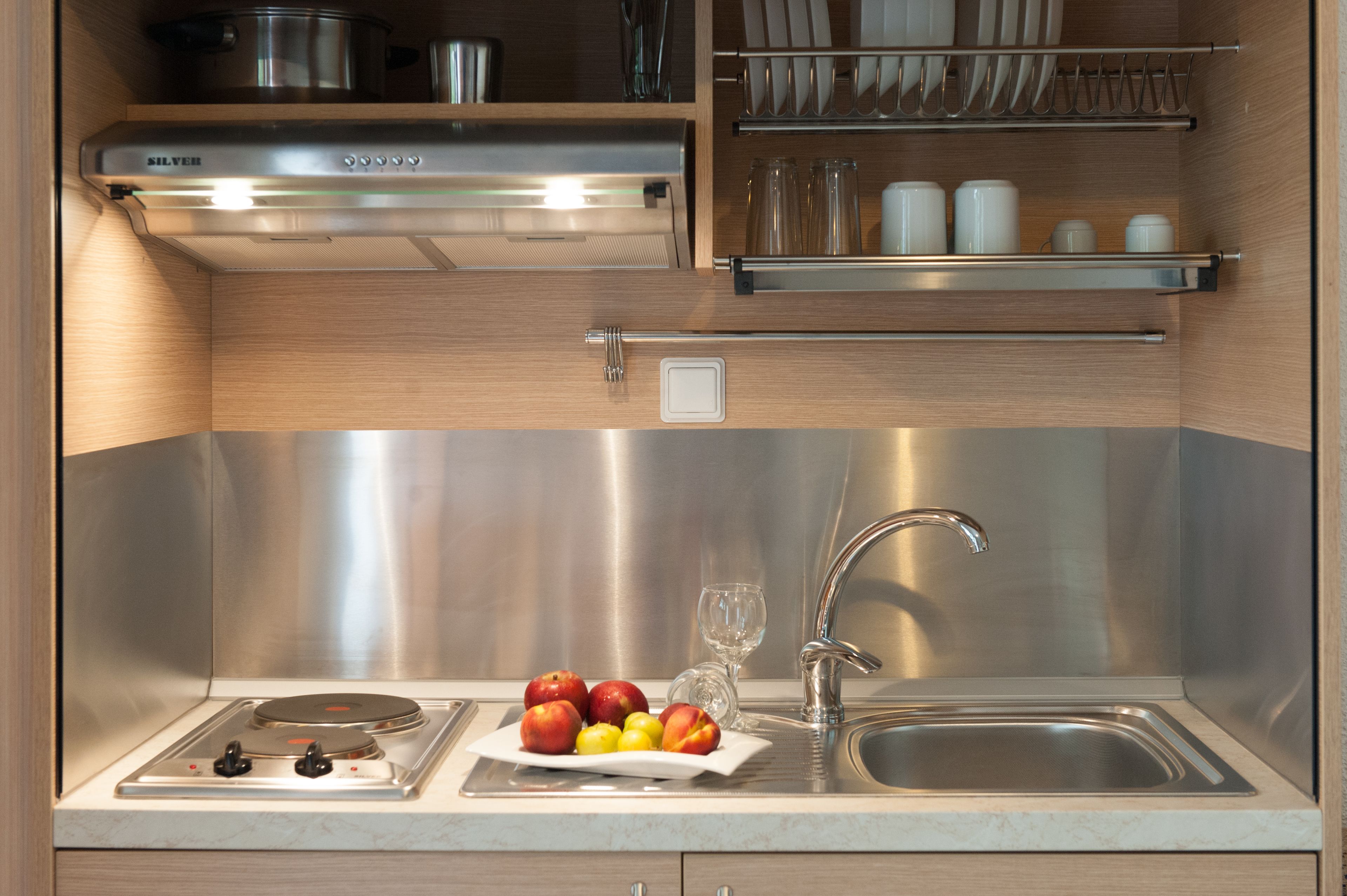 A modern kitchen with stainless steel appliances, a sink, and a fruit bowl with apples and lemons.