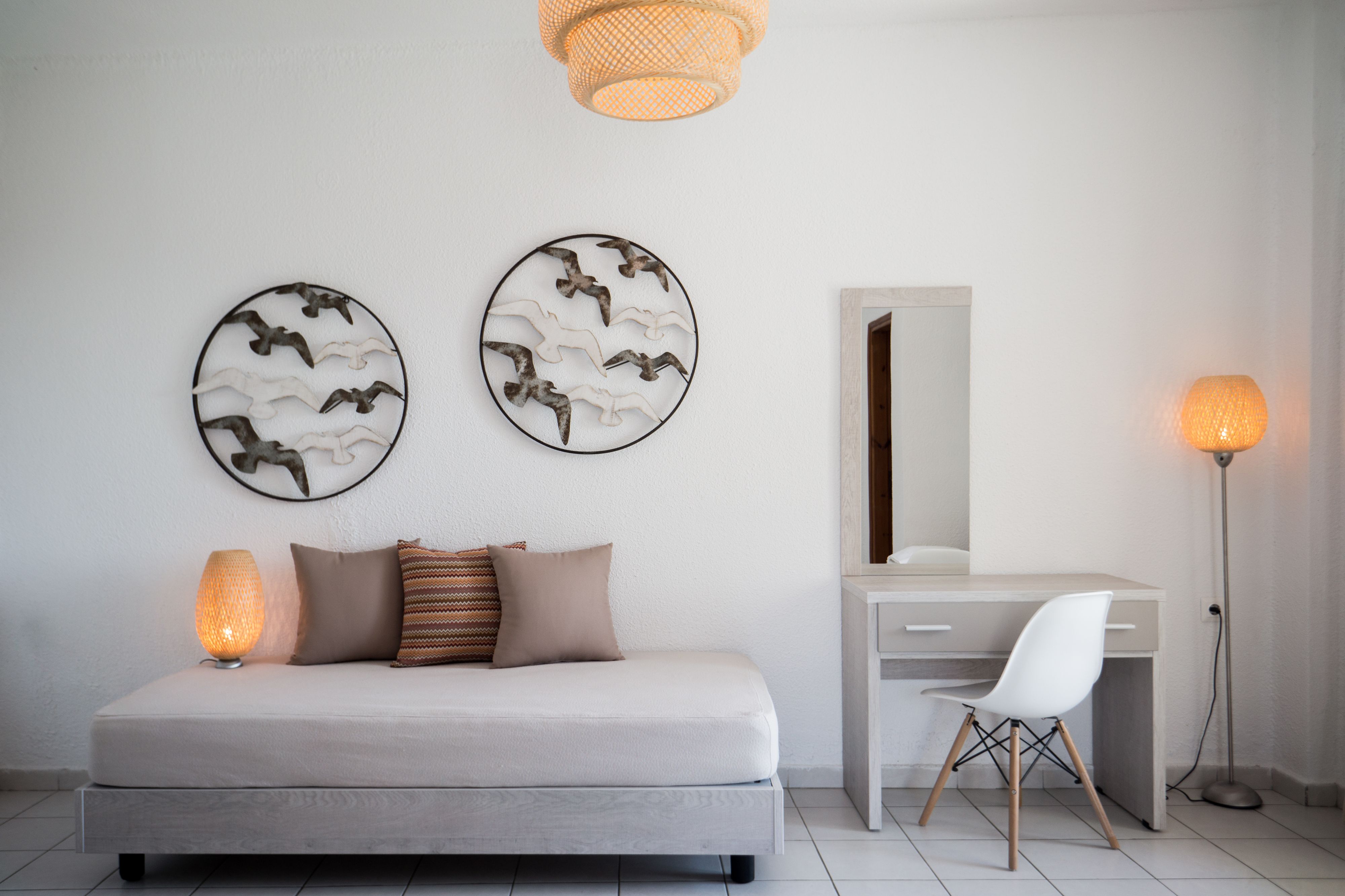 A modern bedroom with a sofa, a desk, and two wall art pieces depicting birds.