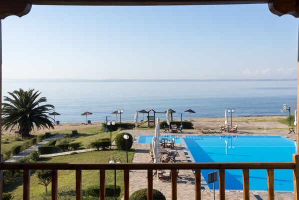 A pool area with a view of the sea, outdoor seating, and a palm tree.
