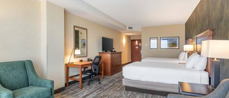 A hotel room with a bed, two armchairs, a desk with a computer, a television, and a dresser.