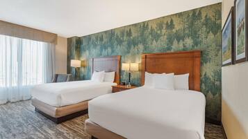 Habitación de hotel con dos camas, un ventanal con cortinas, papel tapiz con motivos forestales y un cuadro en la pared.