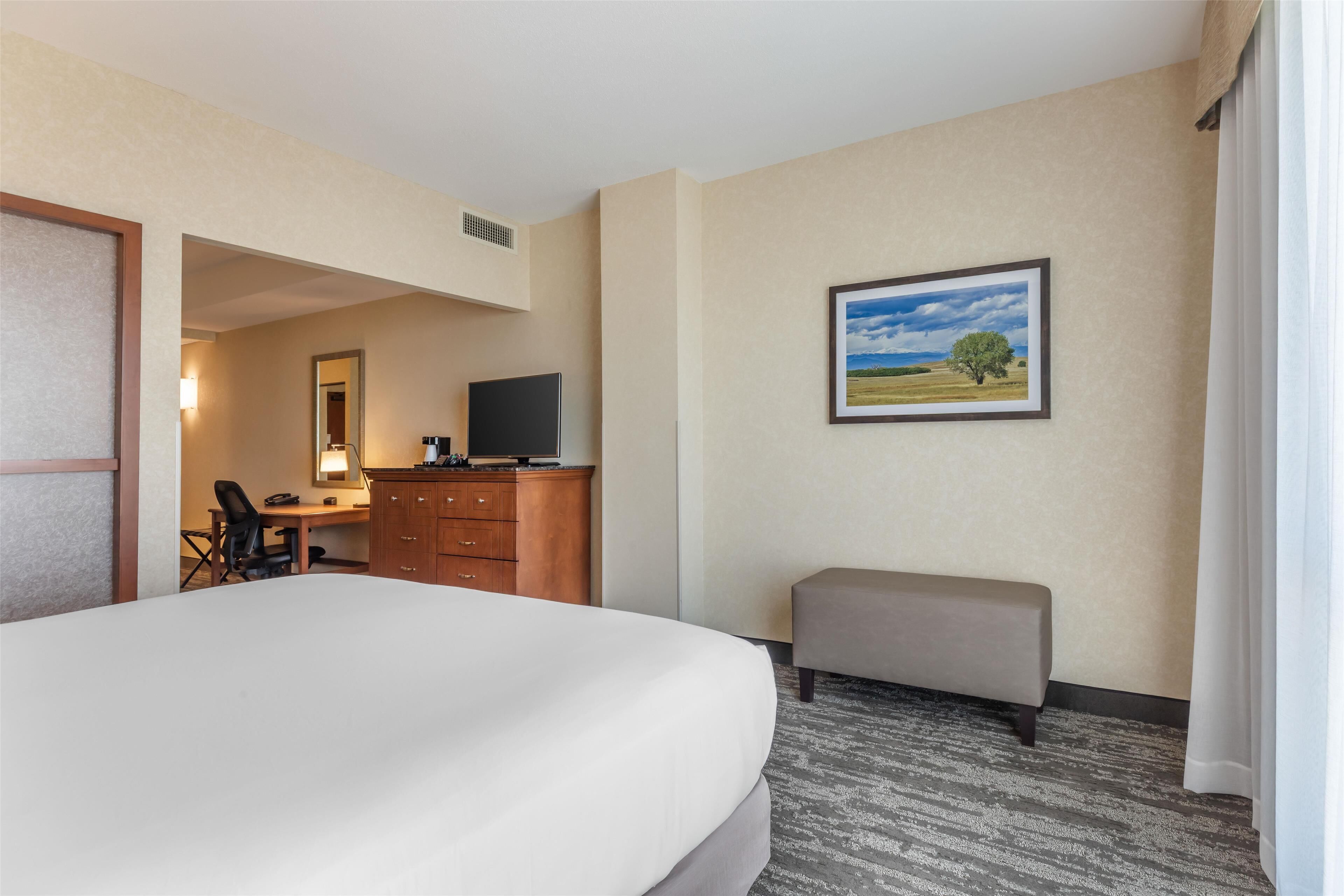 Habitación de hotel con una cama grande, un escritorio con ordenador, televisión y un cuadro de un paisaje en la pared.