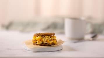 A sandwich on a white plate with a napkin, a white cup, and a spoon in the background.