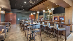 Un área de bar moderna con mostradores de madera, taburetes acolchados e iluminación colgante.