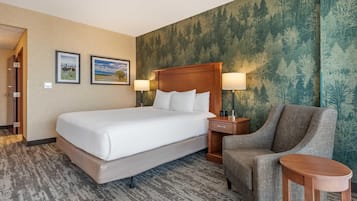 A hotel room with a large bed, two bedside tables with lamps, a chair, and a small table.