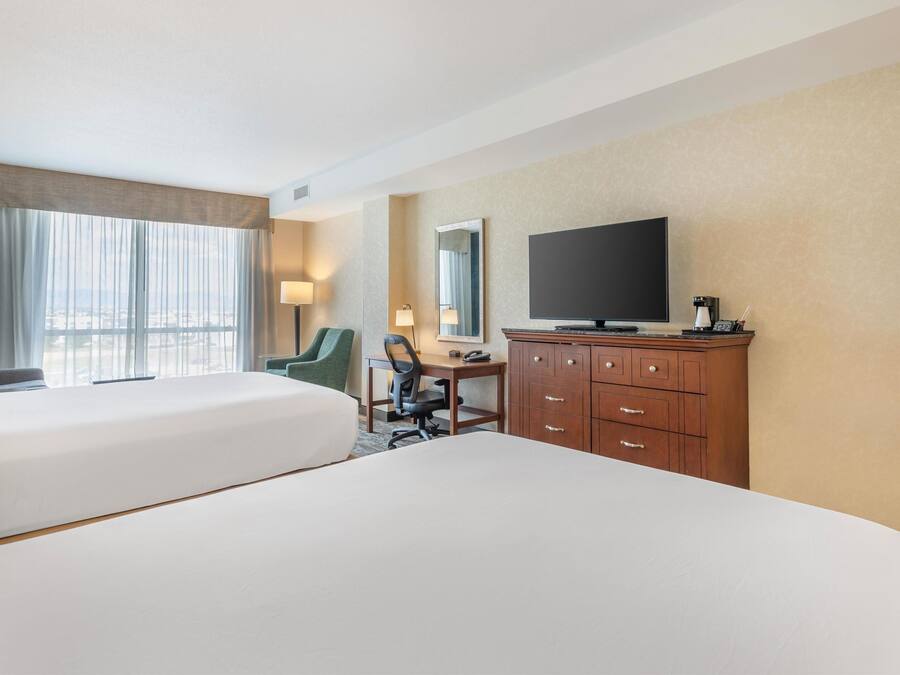 A hotel room with two beds, a desk, a chair, a TV, and a dresser.