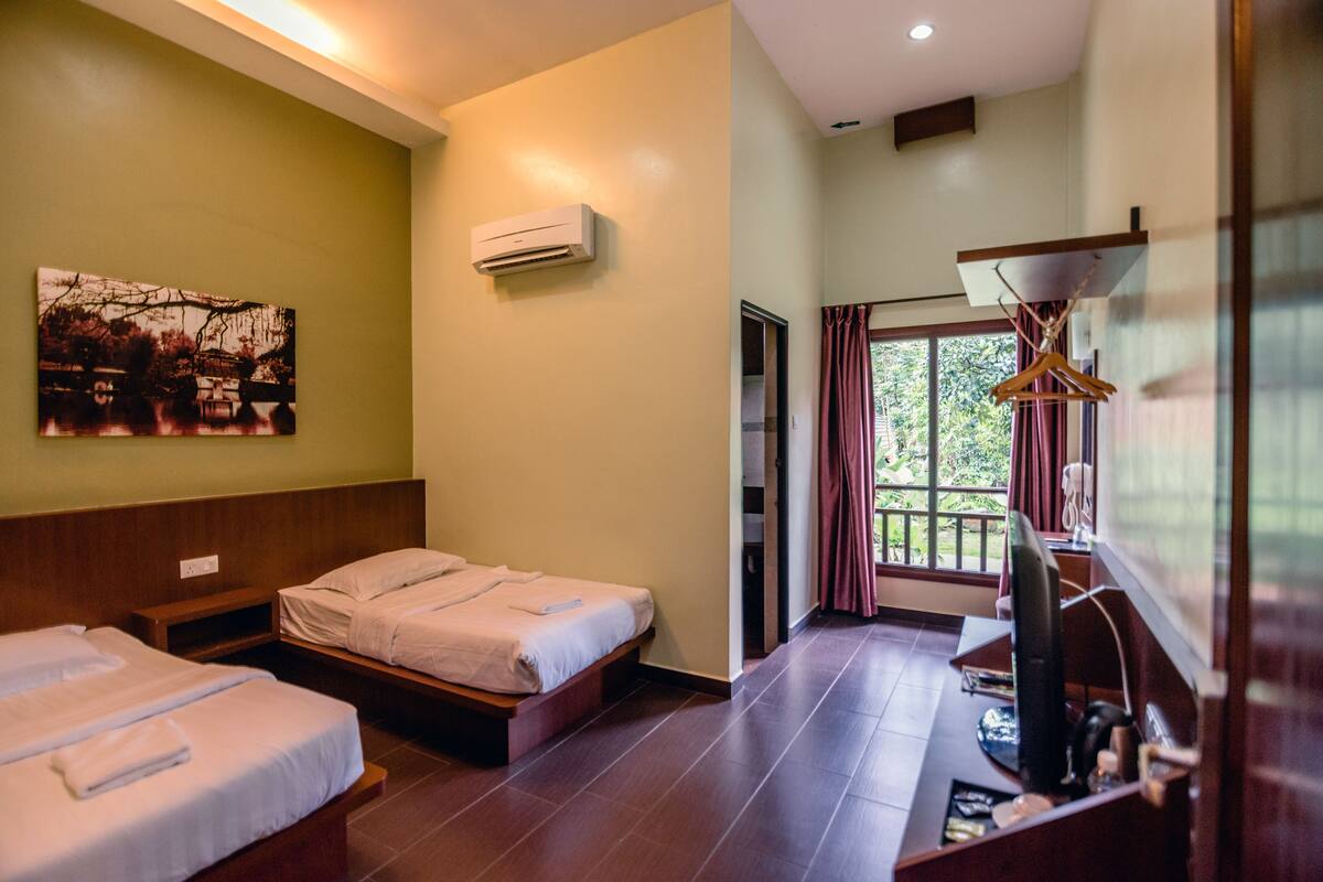 A hotel room with two beds, a flat-screen TV, a wooden bench, and a painting on the wall.