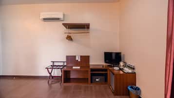 Una habitación compacta con un escritorio de madera, televisión, estante pequeño y un bote de basura.
