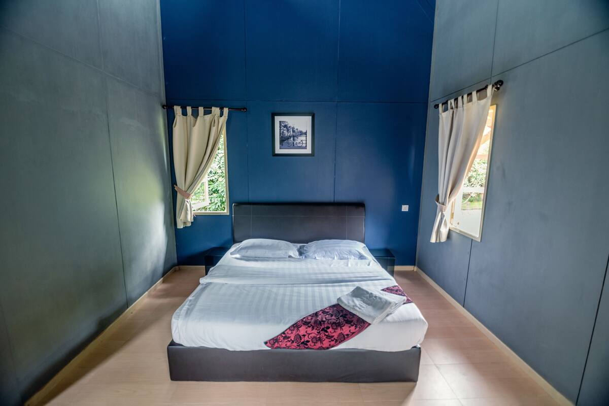 A bed in a room with blue walls, a framed picture on the wall, and a window with curtains.
