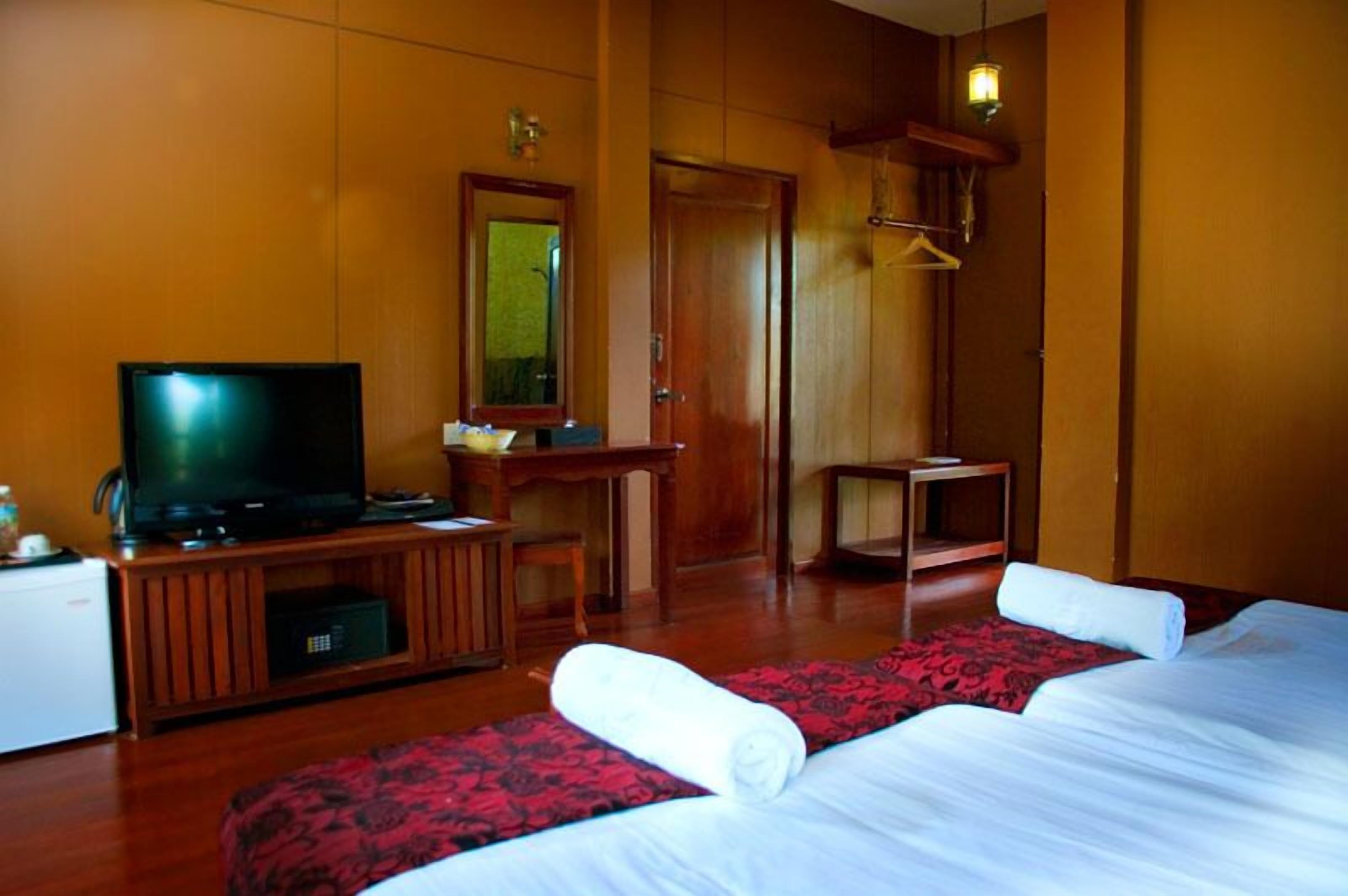 Una habitación de hotel con una televisión, un escritorio, una silla, una cama con colcha estampada en rojo y negro, y un armario de madera.