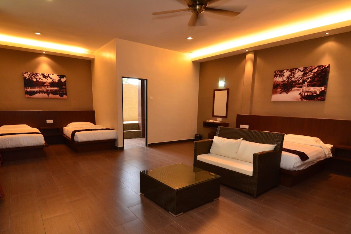 A hotel room with two single beds, a sofa, a coffee table, and a ceiling fan.