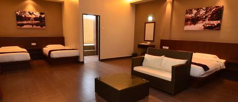A hotel room with two single beds, a sofa, a coffee table, and a ceiling fan.