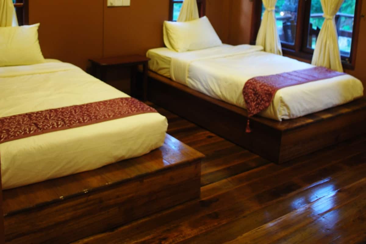 A room with two beds, wooden flooring, and curtains.