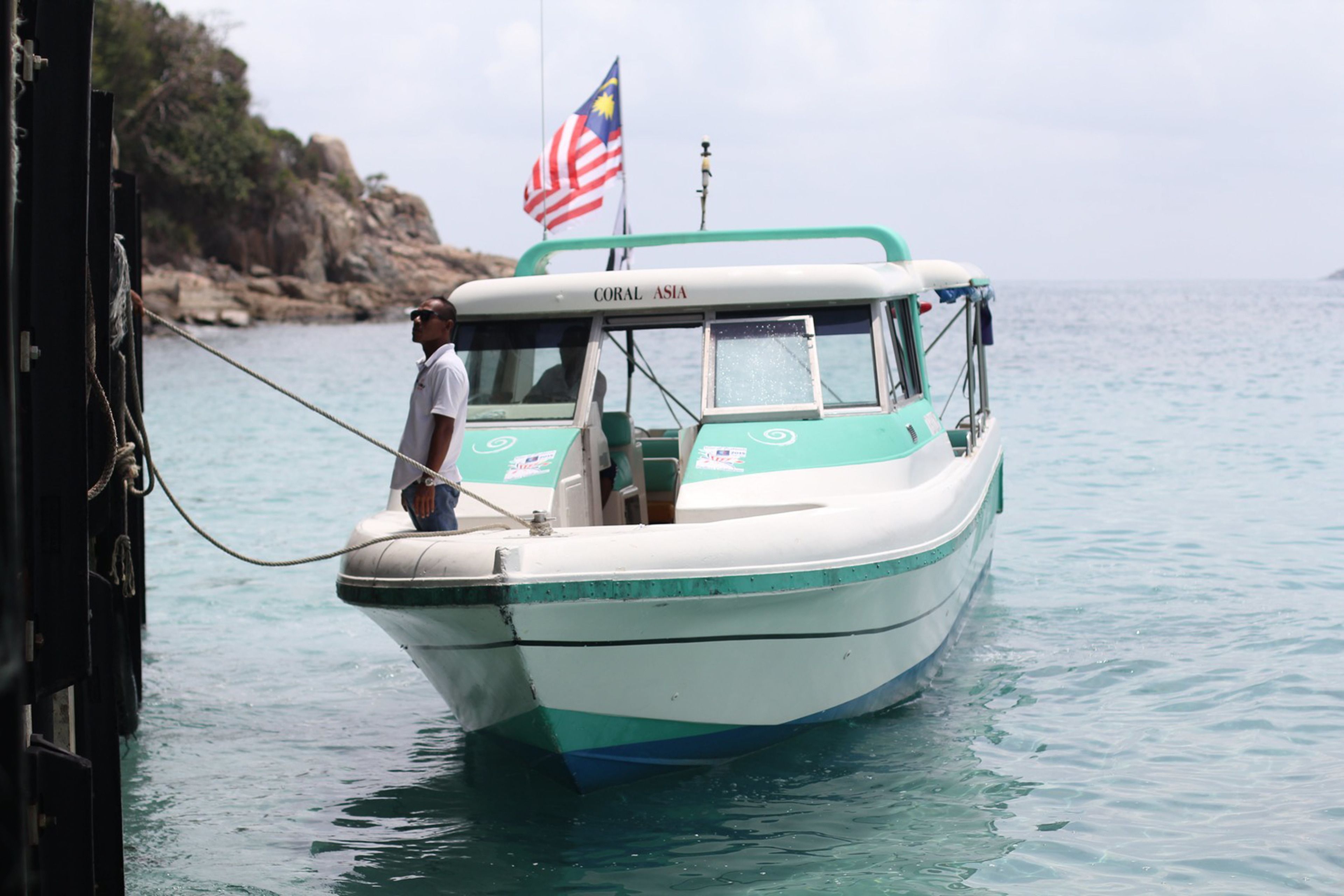 A boat named "CORAL ASIA" with a flag, anchored near rocky terrain.