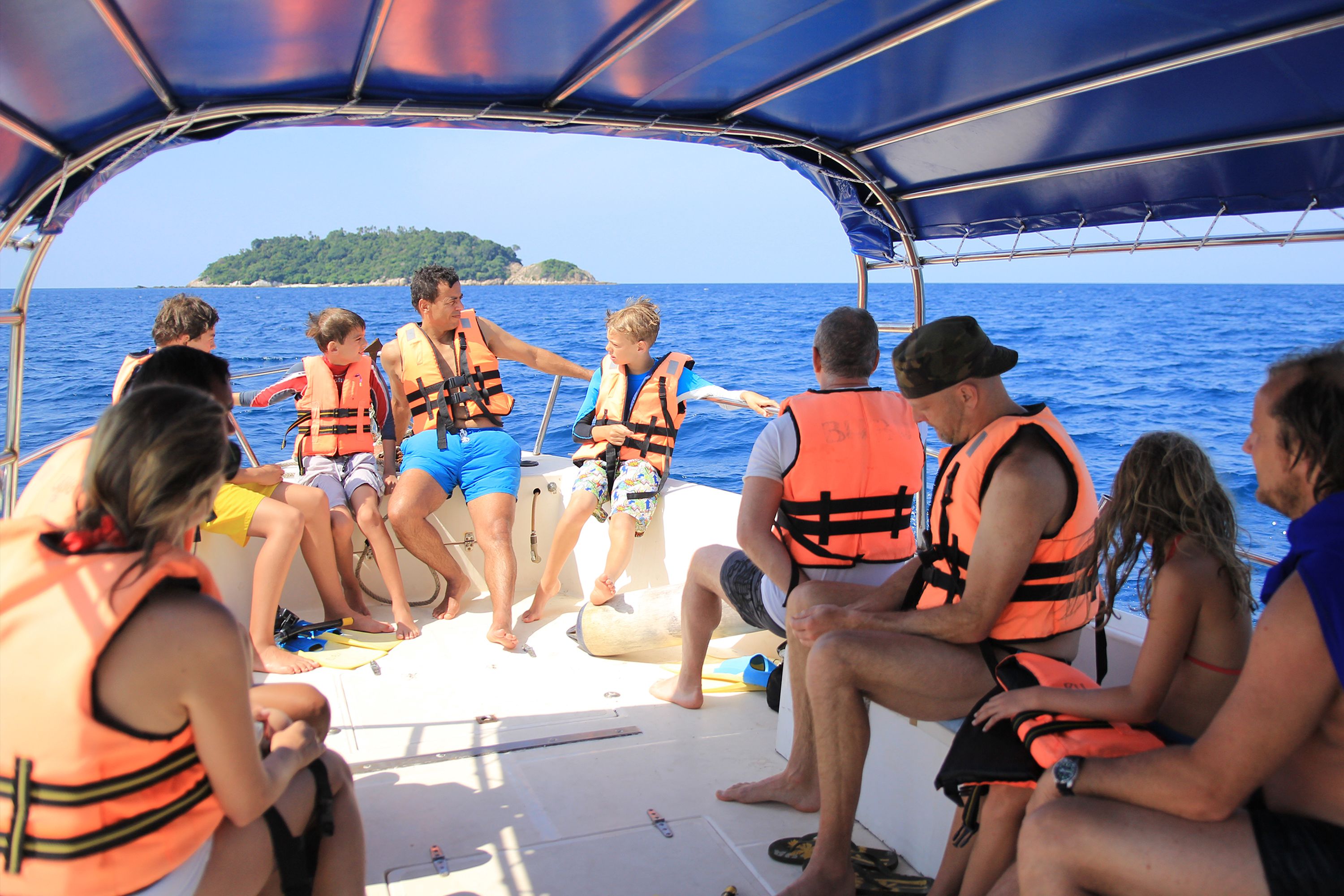 A group of people on a boat wearing life jackets, with a clear view of the sea and a distant island.