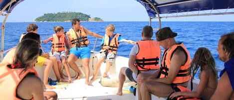A group of people on a boat wearing life jackets, with a clear view of the sea and a distant island.