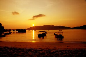 A sunset over a calm body of water with boats and a pier. - BuBu Villa (Pulau Perhentian Kecil)