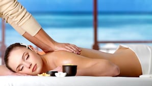 Eine Person bekommt eine Massage auf einer Liege, im Hintergrund ist das Meer zu sehen.