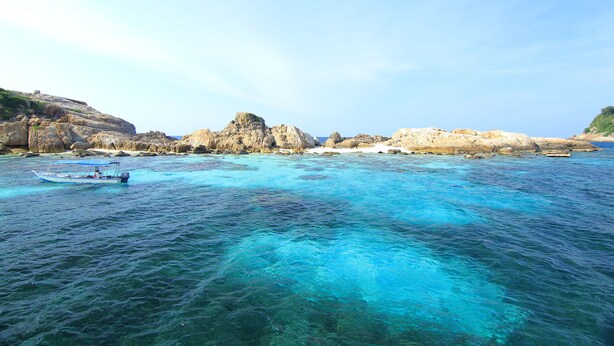 Eine Küstenlandschaft mit klarem türkisblauem Wasser, Felsformationen und einem kleinen Boot.