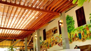 A covered outdoor area with wooden beams, a mural, seating, and a staircase. - Siddhalepa Ayurveda Resort - All Meals, Ayurveda Treatment, Yoga (Wadduwa)