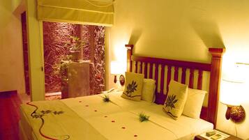 A hotel room with a bed, a nightstand, a lamp, and a view of a garden through a window.