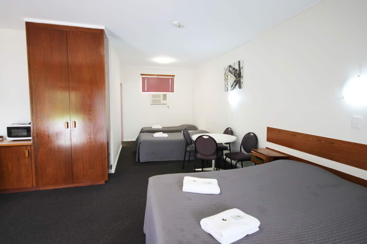 A hotel room with a large wardrobe, two single beds, a small table with chairs, and a microwave on a side table.