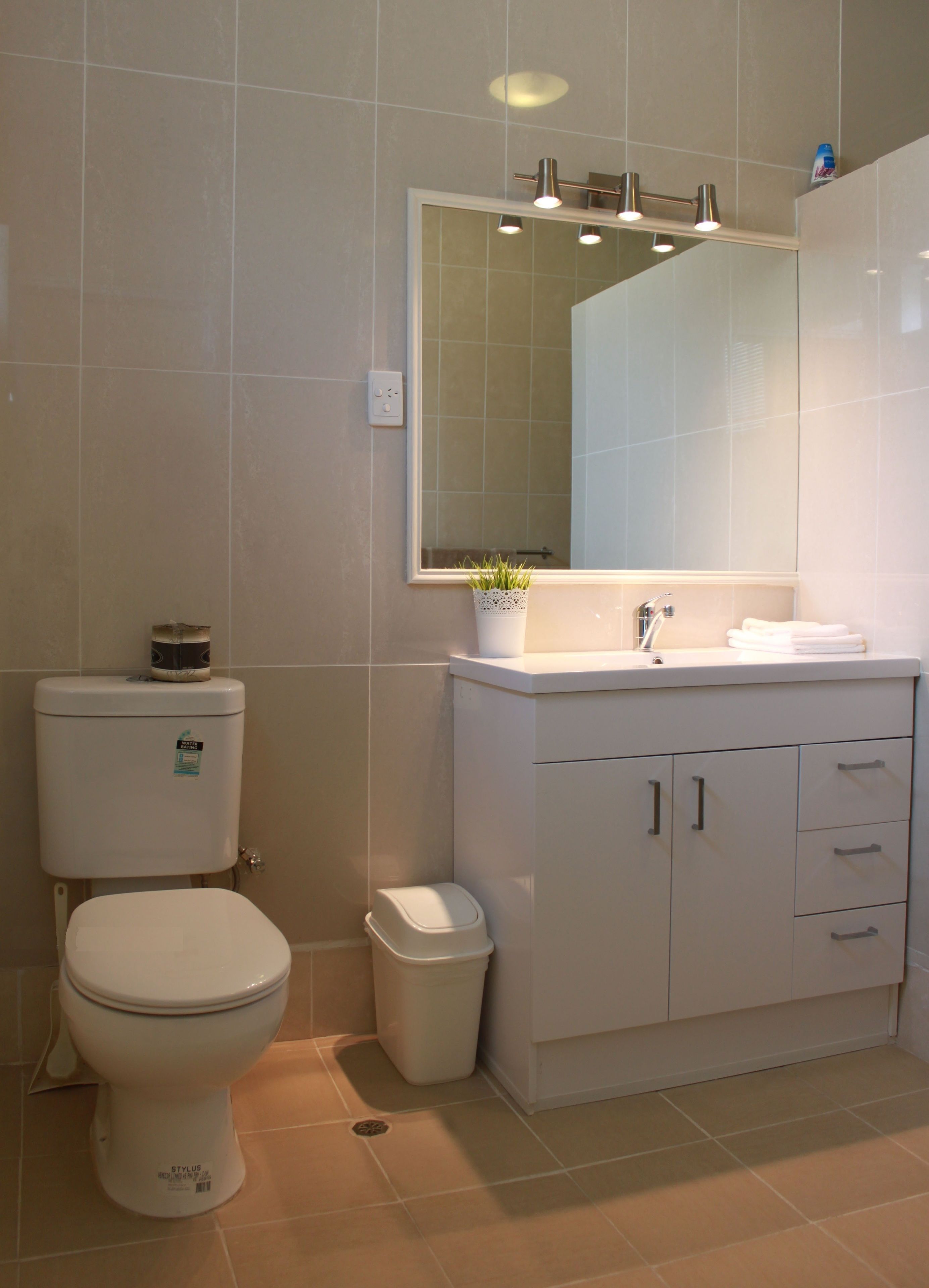 A bathroom with a toilet, a sink, a mirror, and a trash bin.