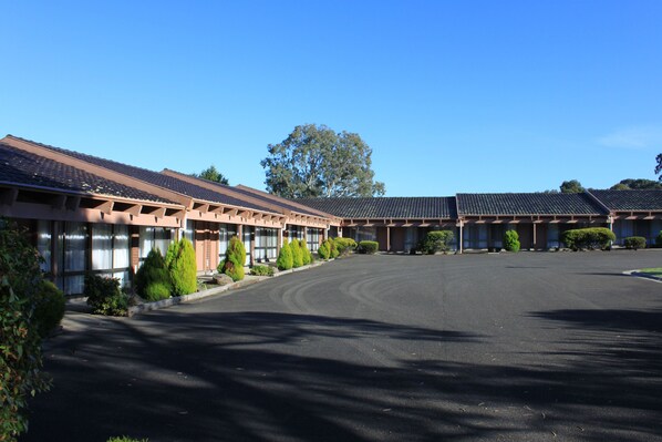A row of motel buildings with a large parking lot in front.