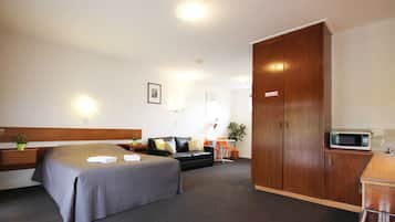 A hotel room with a bed, a sofa, a wardrobe, a desk with a microwave, and a small table with a plant.