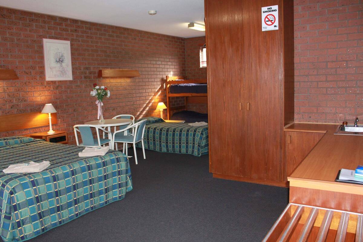 A room with two beds, a desk, a chair, a table, and a no-smoking sign.