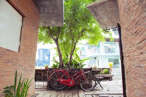 A red bicycle parked against a brick wall, with a bench and potted plants nearby.