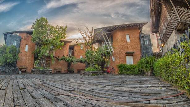 A courtyard with a wooden deck, brick buildings, and a bicycle. - Hy Resort (Chonburi)