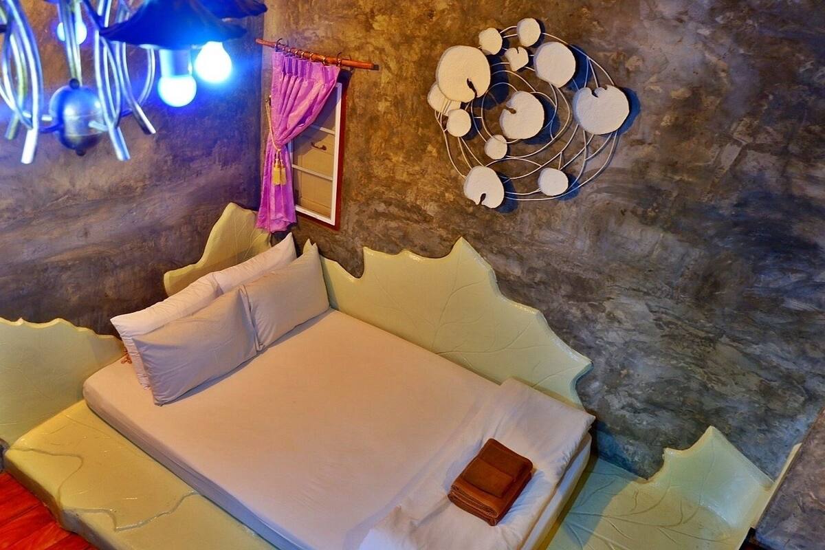 Una cama con colchón y almohadas blancas, cabecera de madera y pared con un diseño original.