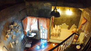 A room with a wooden staircase, a bed with a unique headboard, a table with chairs, and a window with curtains. - Hy Resort (Chonburi)