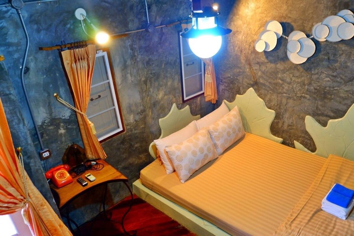 Un dormitorio con cama, mesita de noche, lámpara y espejo adosado a la pared.