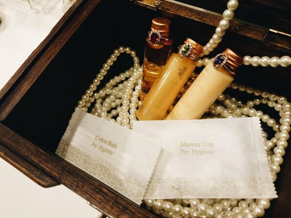 Una caja de madera que contiene un collar de perlas, dos botellas con etiquetas y un pañuelo blanco.