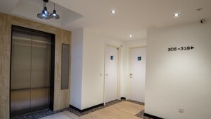 A modern hallway with an elevator, two doors marked with numbers, and a wall with a contact number. - 12FLY Hotel (Kuala Lumpur)