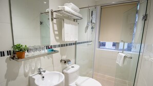 A modern bathroom with a glass-enclosed shower, a white sink, and a toilet. There is a towel rack with towels, a potted plant, and a shelf with toiletries. - 12FLY Hotel (Kuala Lumpur)