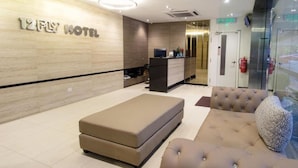 A modern hotel lobby with a reception desk, a seating area with a sofa and ottoman, and a wall-mounted sign reading "12FLY HOTEL". - 12FLY Hotel (Kuala Lumpur)