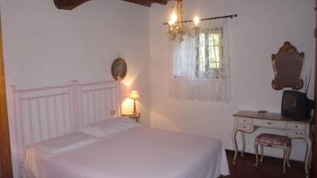 A bedroom with a bed, a desk with a chair, a mirror, and a chandelier.