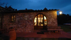 A stone building with a large arched doorway, a bench, and a potted plant outside. - Albergo Il Colombaio (Castellina in Chianti)