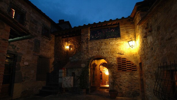 A stone building with an arched entrance, a wooden door, and a small balcony with a railing. - Albergo Il Colombaio (Castellina in Chianti)